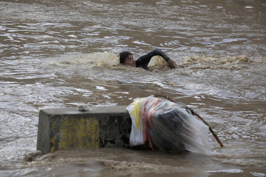 na persona nada a través del agua de una inundación después de fuertes lluvias en Sana'a, Yemen