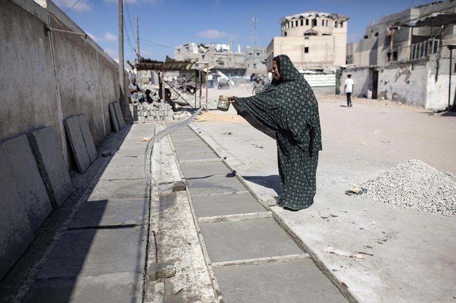 La palestina desplazada Hayat Abu Hatab rocía agua sobre las lápidas que hizo con piedras recogidas de casas destruidas por ataques aéreos israelíes anteriores