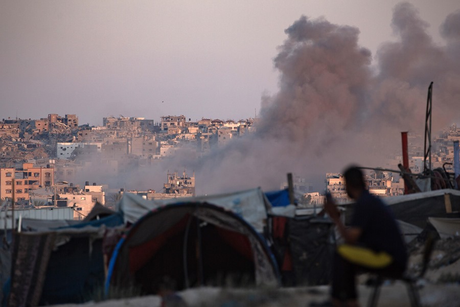 El humo se eleva tras un ataque aéreo israelí mientras los palestinos desplazados internos se sientan junto a sus tiendas de campaña en el campamento de Khan Younis