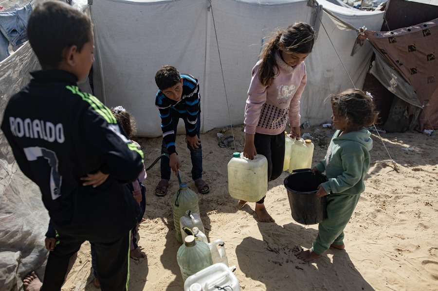 Niños palestinos llenan unos bidones con agua en un campamento para desplazados