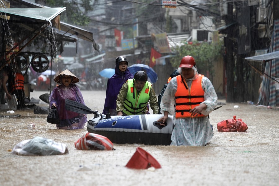 Varias personas empujan un bote inflable por una calle inundada de Hanoi, Vietnam