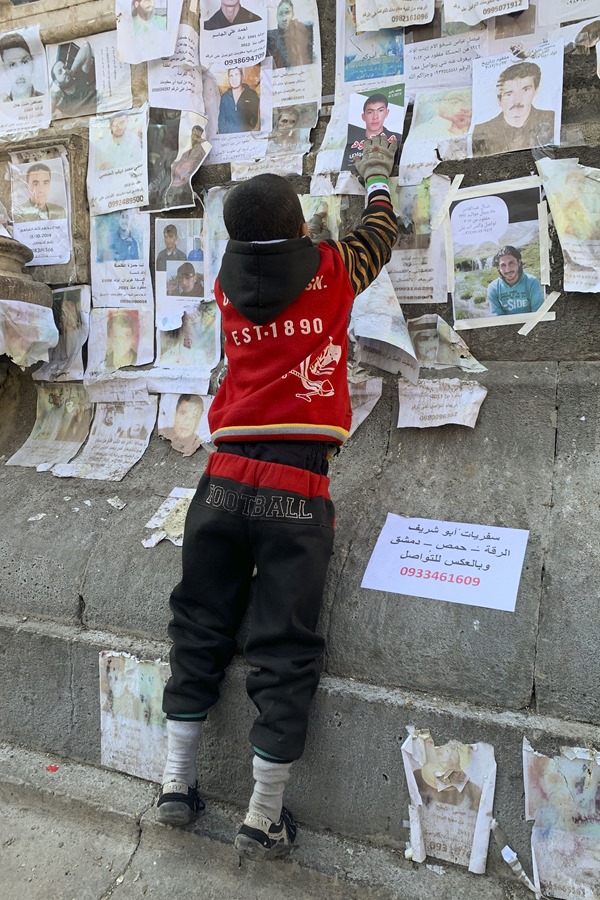 Un niño coloca una foto de un familiar desaparecido aún en paradero desconocido, un mes después del derrocamiento del régimen sirio, en una plaza de Damasco